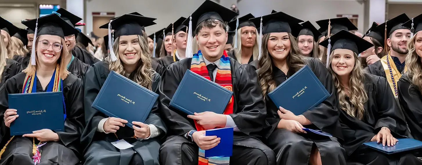 Students posing at commencement with their diploma cover